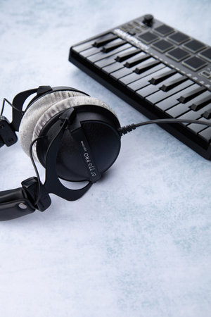 Closed-back headphones of the beyerdynamic dt 770 brand lie next to the AKAI MPK mini mk2 midi keyboard, on a light backgroundのeditorial素材