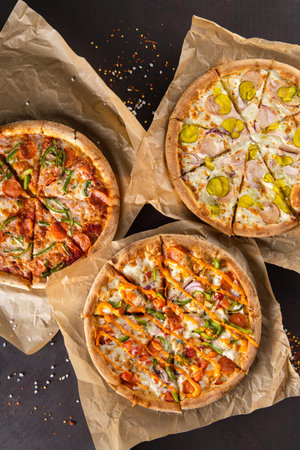 three beautiful colorful juicy different pizzas lie on parchment on a black backgroundの写真素材