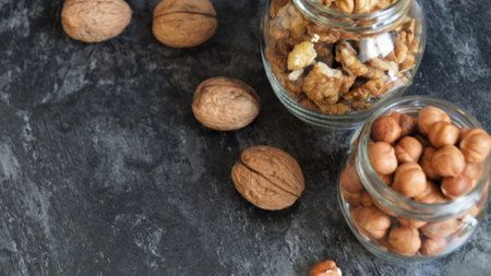 Walnuts and hazelnuts in a glass jar on a black stone backgroundの写真素材