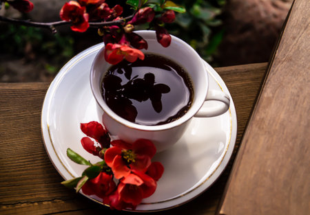 Cup of coffee with red flowers on a wooden table in the gardenの写真素材