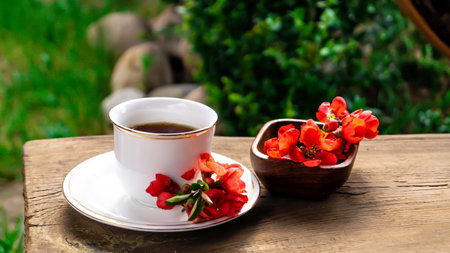 Cup of coffee with red flowers on a wooden table in the gardenの写真素材