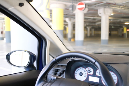 Close up of a steering wheel and instrumentation of a car the background in the parking lot of a mall.の写真素材