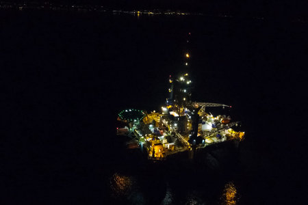 Drilling platform in the port. Oil platform at night in the light of its own lighting. Towing of the...