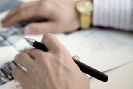 Men's hands with gold watches hold a writing pen over the paper.の写真素材