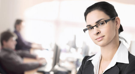 Businesspeople work in the office while a businesswomen stands in the foreground.