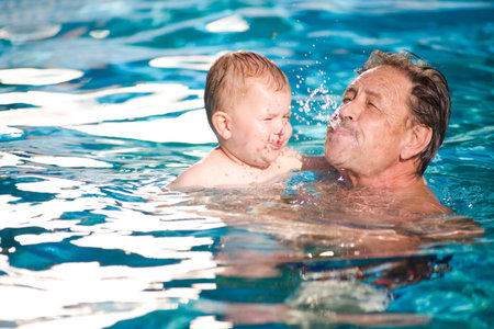 Grandfather and grandson playing together in the pool. Outdoor, summer.の写真素材