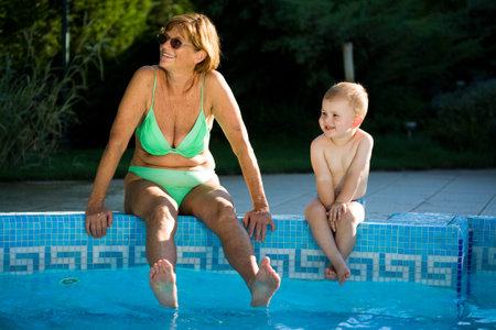 Grandmother and two years old granson enjoy water and sunshine on the poolside. Natural light, summer.の写真素材