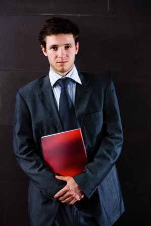 Portrait of satisfied young businessman in grey suit standing at office corridor.