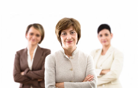 Happy businessteam of three businesswomen standing in front of windows inside officebuilding, smiling, senior businesswoman leading. Isolated on white.の写真素材