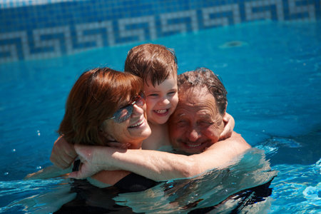 Happy family: grandparents having bath in pool together with grandson (3 years), smiling, outdoor, summer.の写真素材