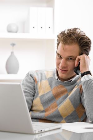 Young man using laptop and calling on phone at home.の写真素材