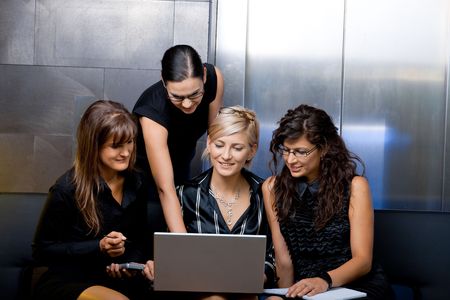 Team of attractive businesswoman having a meeting sitting on couch, using laptop computer, smiling.の写真素材