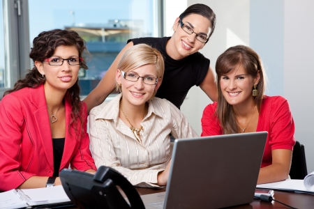 Team of  young businesswomen using laptop computer  in meeting room. Looking at camera, smiling.の写真素材