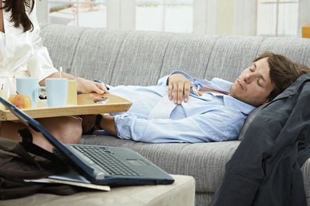 Young businessman resting on couch, woman holding breakfast tray.の写真素材