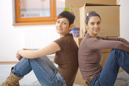 Two young women sitting on floor, exhausted by moving cardboard boxes to new home.の写真素材
