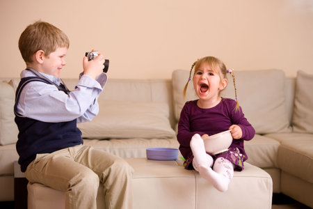 Young boy sitting on couch, taking a picture of his happy little sister,