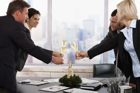 Business people raising toast over meeting table with Christmas decoration at office. Focus placed on flutes in front.の写真素材