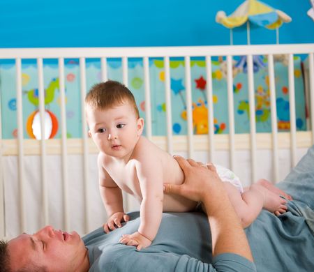 Father lying on back and lifting baby boy ( 1 year old ) at home in children's room.の写真素材