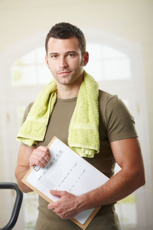 Man wearing sportswear standing in living room at home, holding training plan.の写真素材