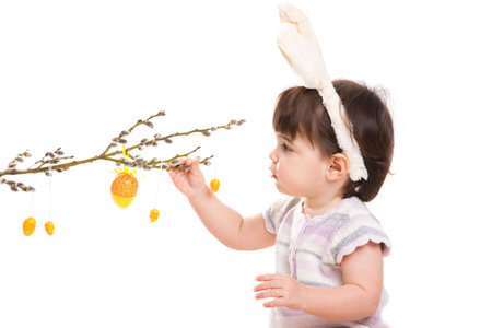 Baby girl in easter bunny costume, playing with easter eggs hanging from willow branch. Isolated on...