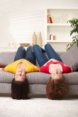 Teen girls lying on couch upside down, listening to music in earbuds, eyes closed.の写真素材