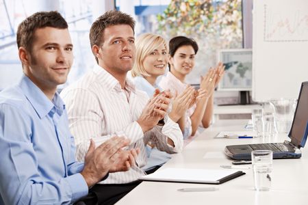 Happy business people sitting at table in meeting room clapping listening to presentation.の写真素材