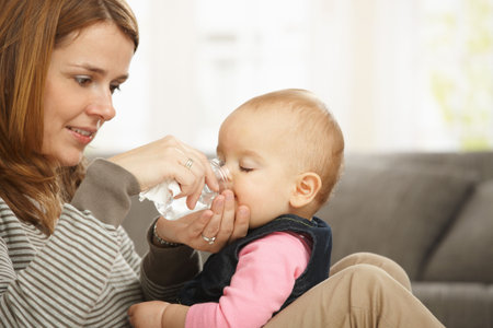Happy mum holding baby girl in arms smiling baby drinking from feeding bottle.の写真素材