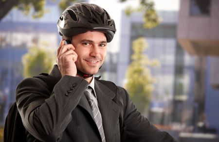 Portrait of young businessman wearing bike helmet, talking on mobile phone, outdoors.の写真素材