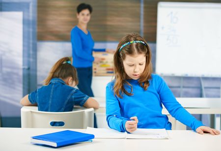 Schoolgirl thinking while filling out test at class, teacher standing in background.の写真素材