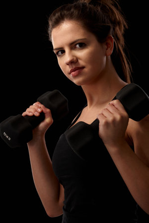 Sporty girl doing exercise with dumbbell looking at camera.の写真素材