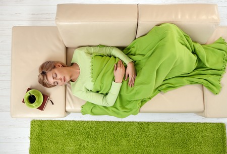Sleeping woman in high angle view lying on sofa under blanket. の写真素材