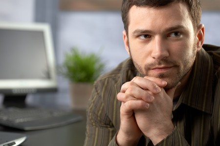 Determined office worker sitting at desk, thinking.の写真素材
