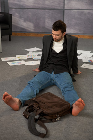 Trendy office worker sitting on office floor bare feet, surrounded with papers, documents and  laptop bag.の写真素材