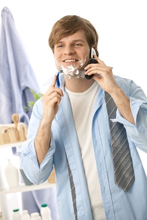Young man talking on mobile while shaving. Isolated on white.の写真素材