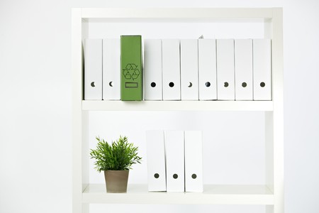 Conceptual image of environmental conservation, green folder with recycling symbol on a shelf full of white folders.の写真素材