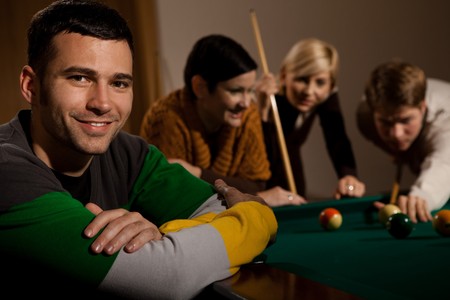 Portrait of smiling young man at snooker table, friends playing in background.の写真素材