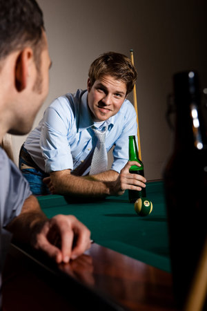 Friends chatting at snooker table, having beer, smiling. 