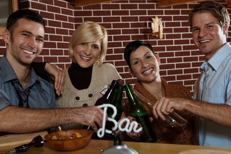 Happy couples celebrating, clinking beer bottles in pub, smiling at camera.