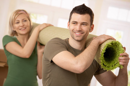 Happy couple carrying carpet together at moving house.の写真素材