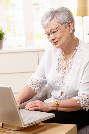 Senior woman browsing internet on laptop at home, smiling.