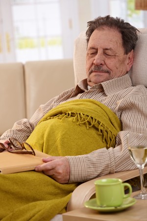 Senior man lying in armchair at home, sleeping in afternoon sunlight.の写真素材