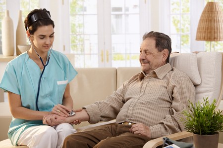 Nurse using stethoscope and measuring blood pressure of senior man at home. の写真素材