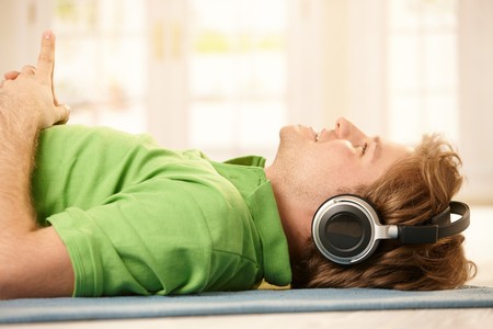 Young man lying on floor wearing headphones, pointing up, smiling.の写真素材