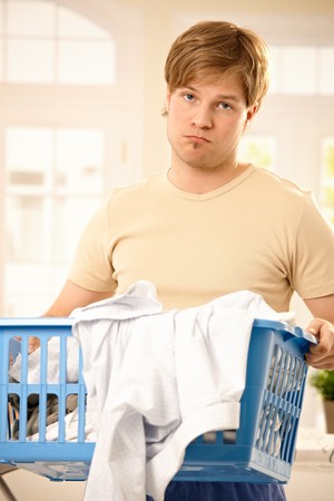 Young troubled guy standing holding washing basket, bored of housework, looking at camera.の写真素材