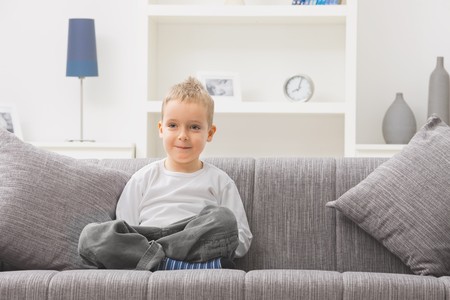 Portrait of little boy wearing white t-shirt, sitting at couch, looking at camera, smiling.の写真素材