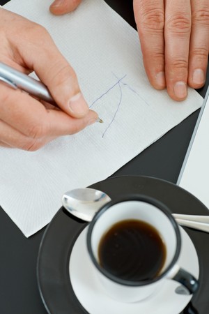 Hands of businessman drawing graph on paper napkin with pen, beside a cup of coffee on table.の写真素材