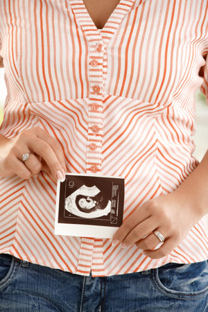 Picture of pregnant woman's tummy, ultrasound baby photo handheld in front. 