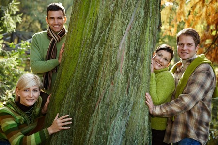 Portrait of four friends standing around huge tree in forest, smiling, looking at camera.の写真素材