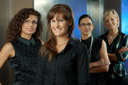 Team of attractive young businesswomen, waiting for lift in corporate ofiice lobby, smiling.の写真素材