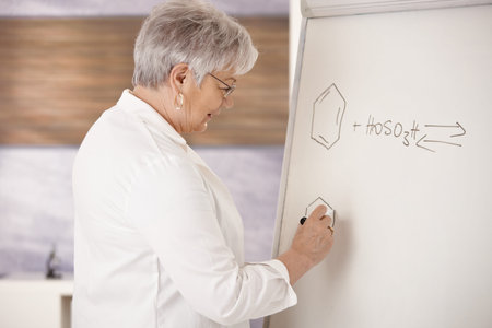Senior teaching chemistry in school, drawing molecular formulas on whiteboard. 